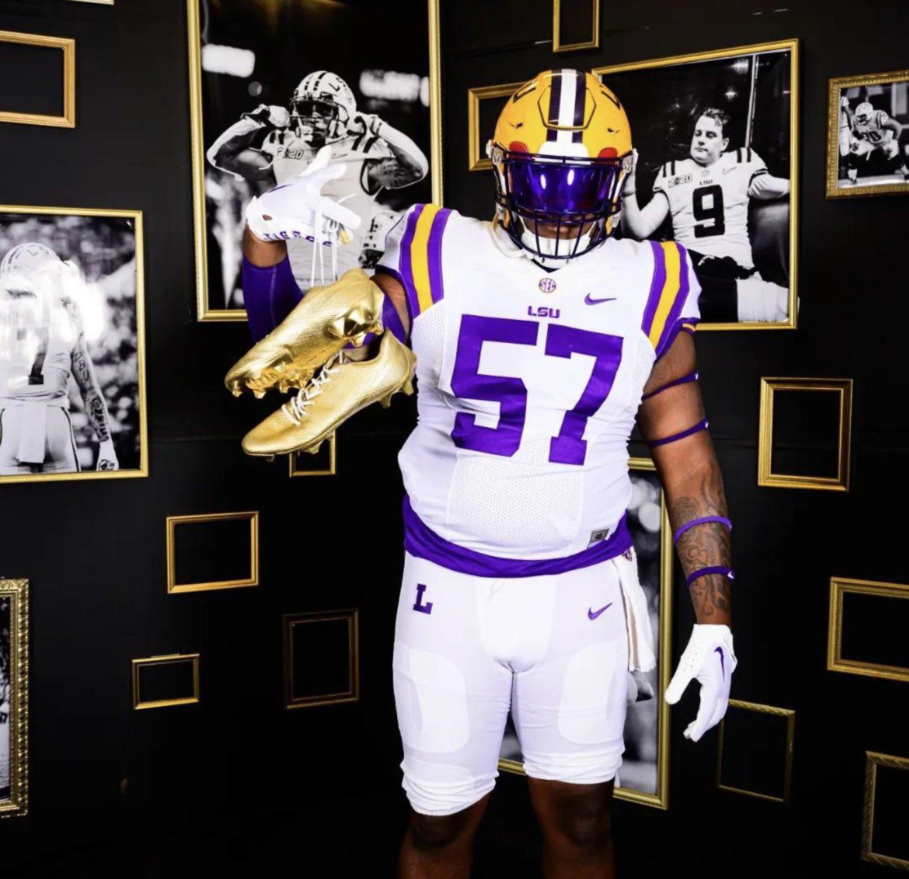 Football player in LSU uniform holding gold cleats.